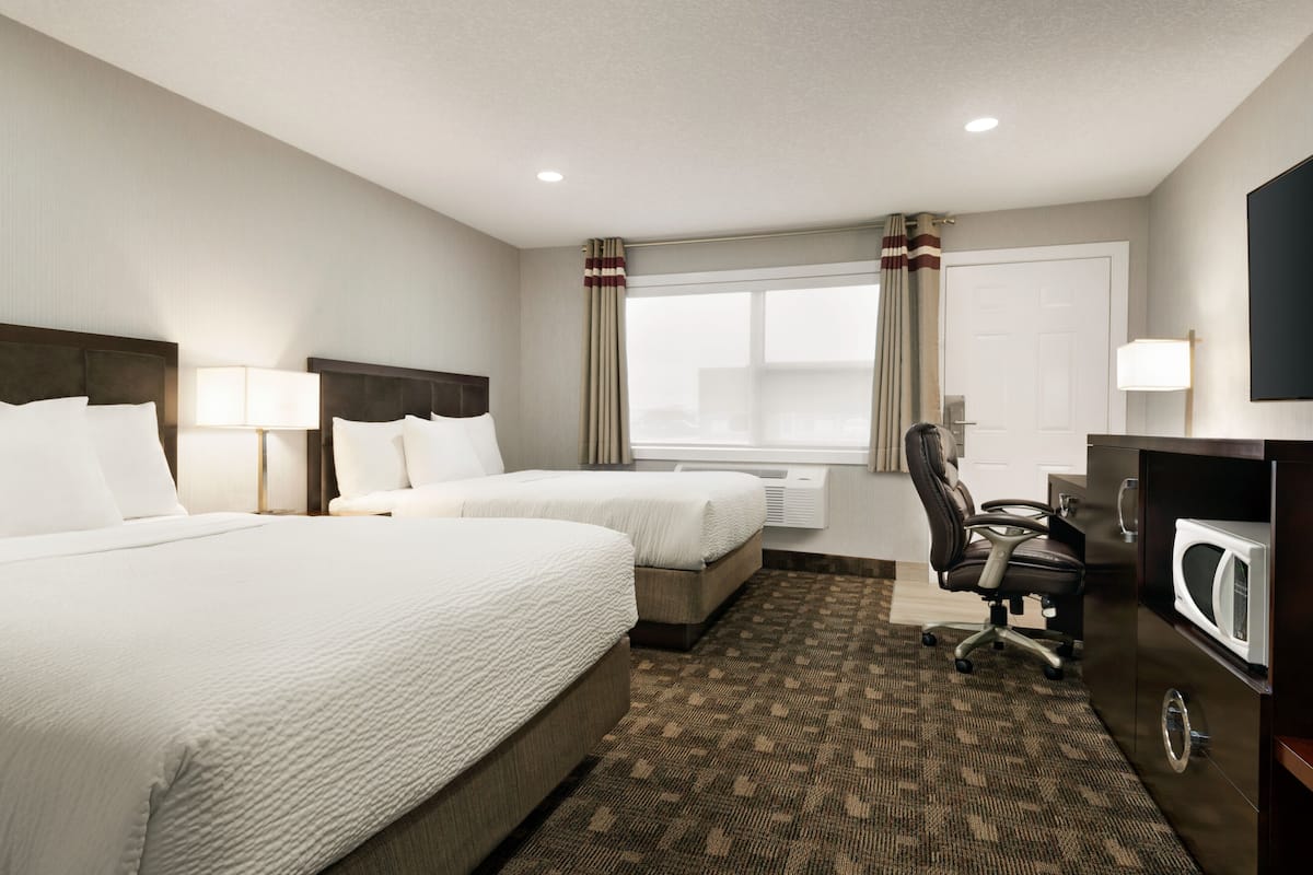 A hotel room with two beds, a desk, a chair, a microwave, and a window with curtains.
