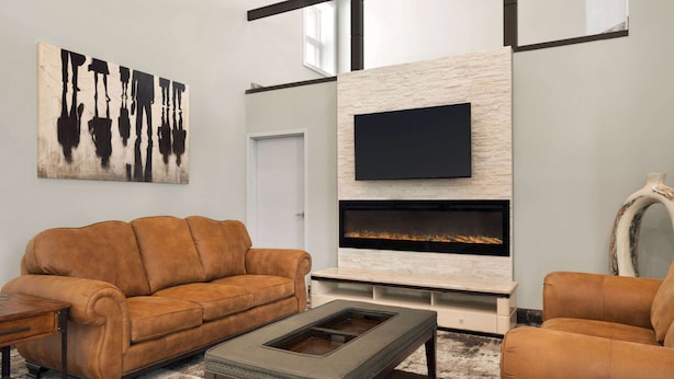 A modern living room with a leather sofa, a coffee table, a flat-screen TV mounted on a stone wall, and a fireplace. - Days Inn by Wyndham Wainwright (Wainwright)
