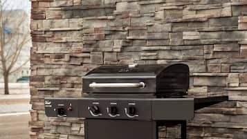 A gas grill with a control panel, set against a stone wall.