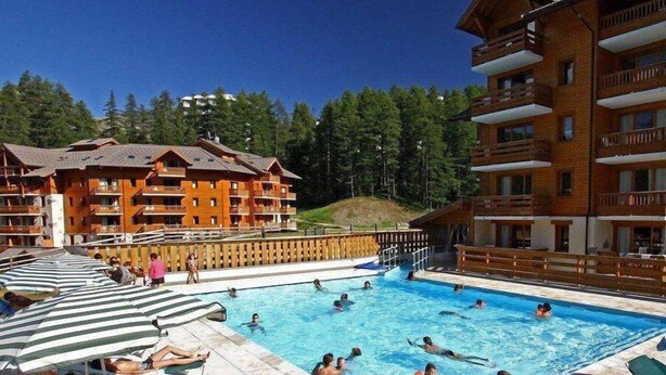 Una piscina rodeada de edificios de madera con balcones, con árboles en el fondo.