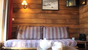 Una habitación de cabaña acogedora con pared de madera, un sofá con cojines a rayas, una mesa con tetera y tazas, una lámpara y un cuadro enmarcado en la pared.