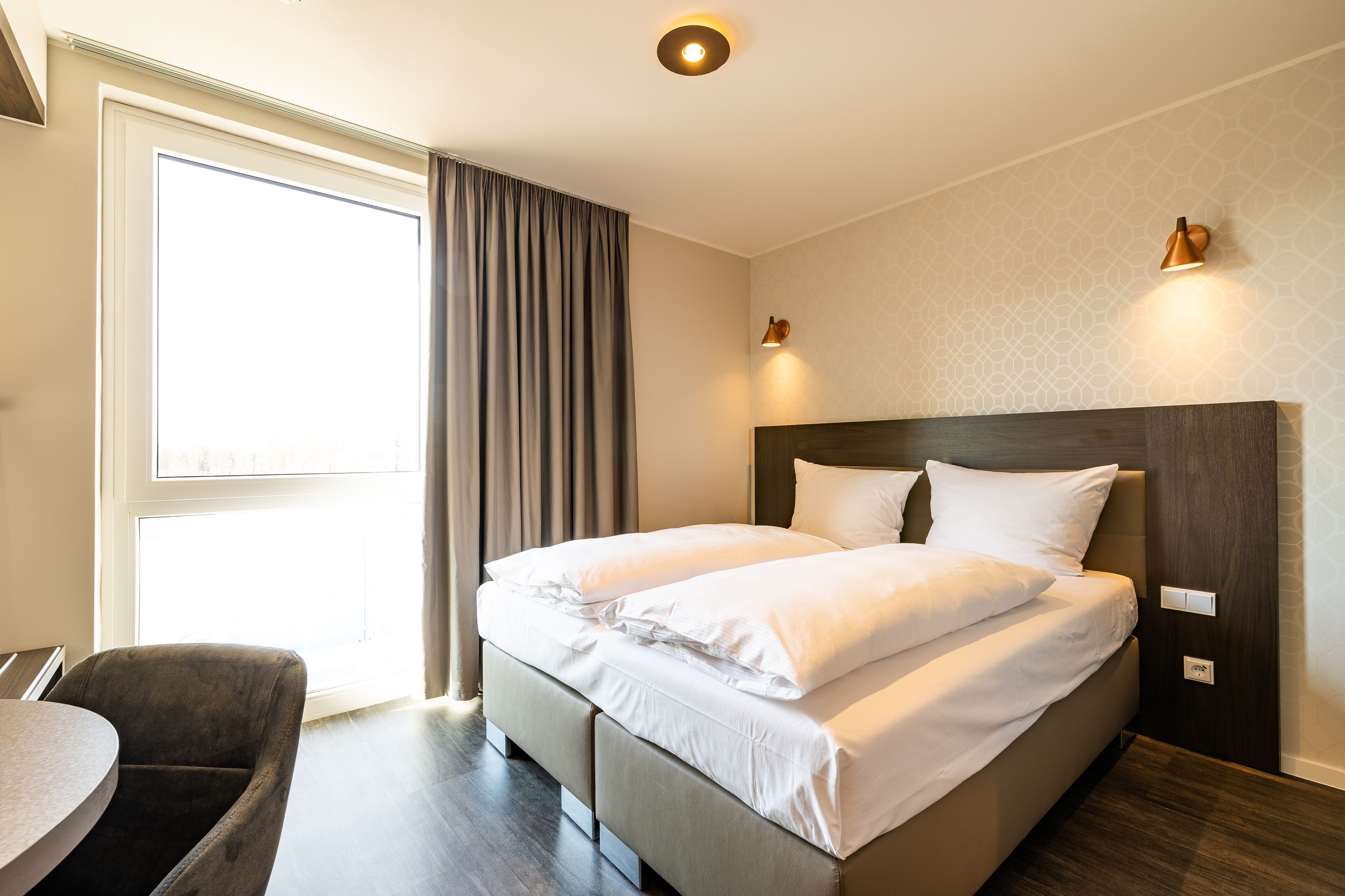 Une chambre d’hôtel moderne avec un grand lit, un bureau et une fenêtre avec des rideaux.