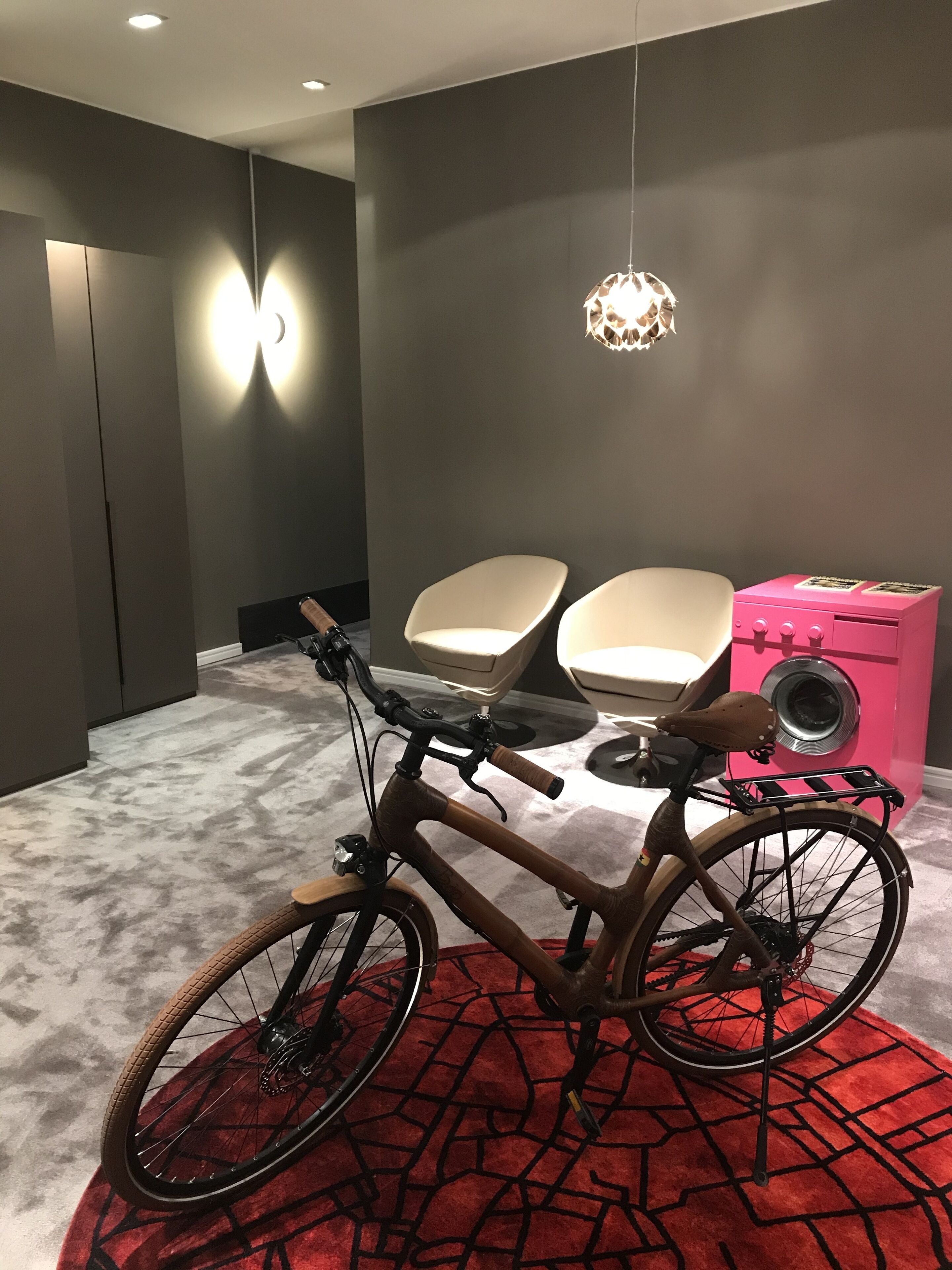Une pièce moderne avec un vélo, deux chaises, une armoire rose et un tapis rouge à motifs.