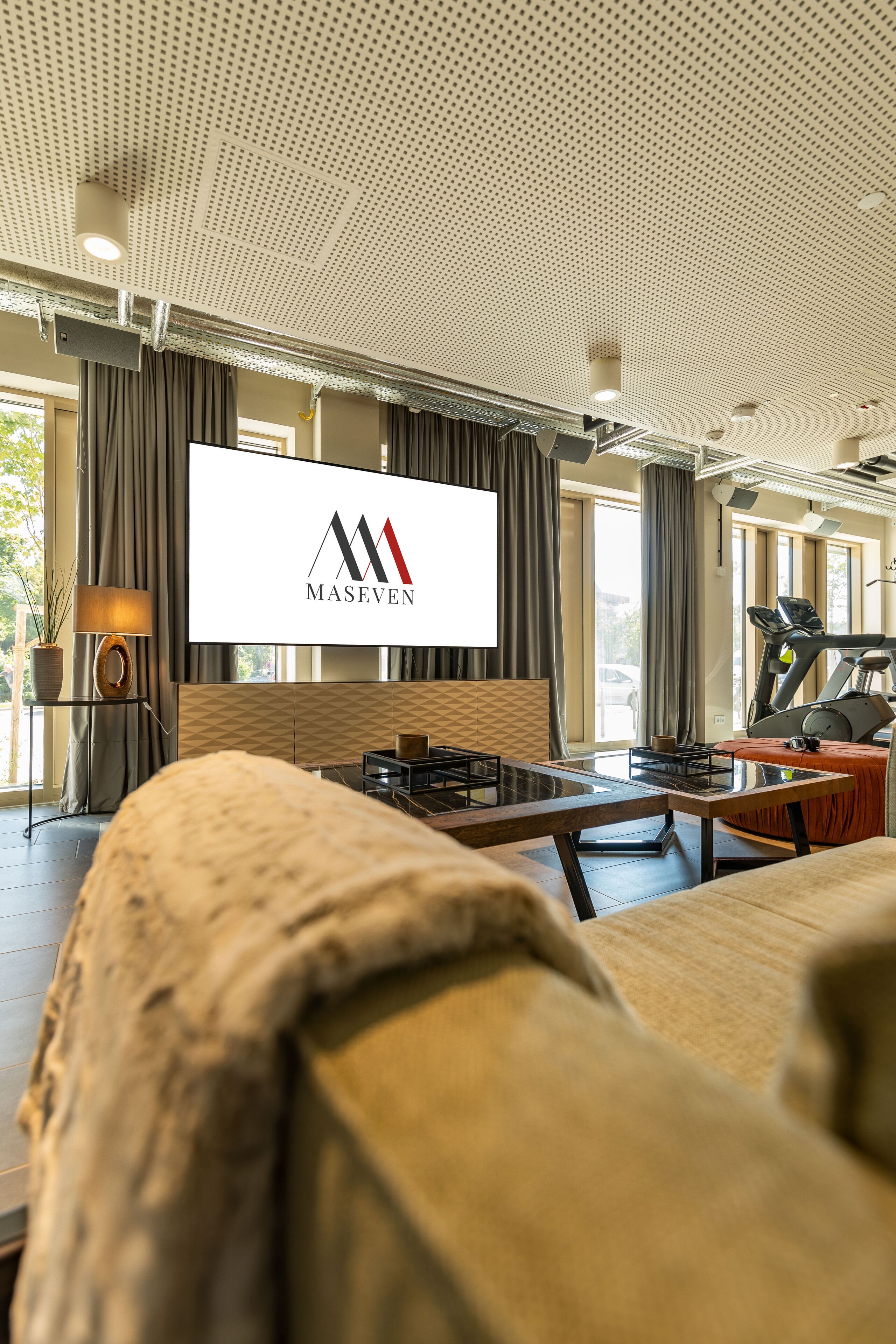 Ein modernes Hotelzimmer mit großem Flachbildfernseher, Trainingsgeräten und einer gemütlichen Sitzecke.
