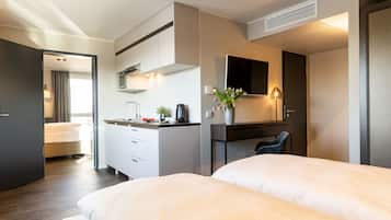 Une chambre d’hôtel moderne avec un grand lit, un bureau, un téléviseur à écran plat, une petite plante et une vue sur la salle de bain.