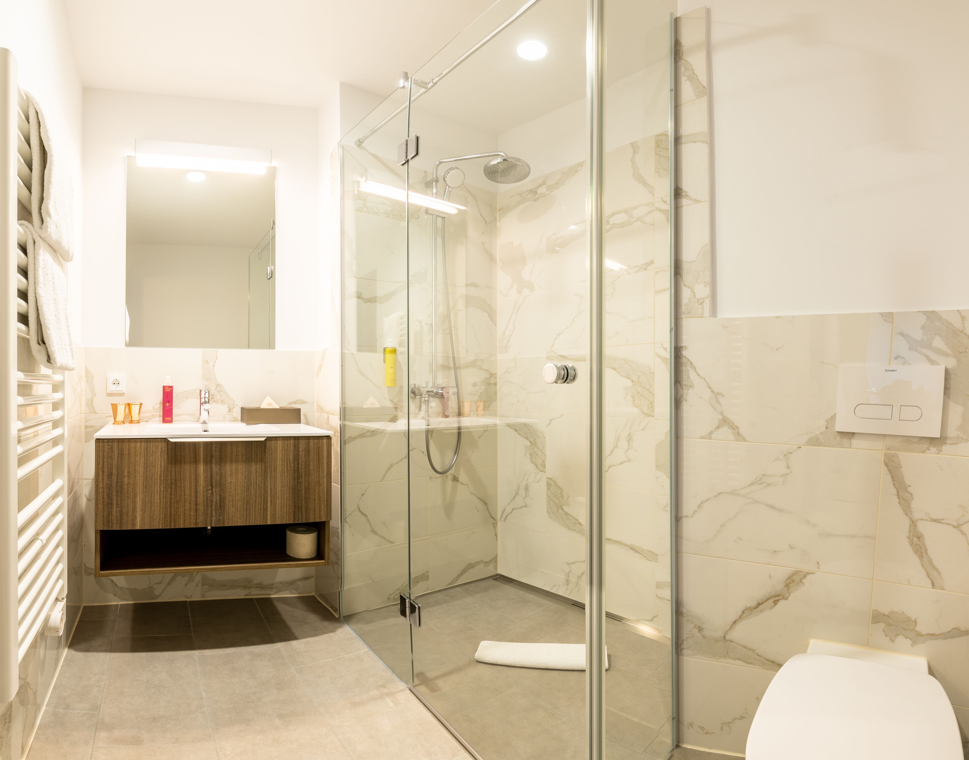 A modern bathroom with a glass-enclosed shower, a wooden vanity, and a marble-tiled wall.