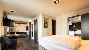 A modern hotel room with a large bed, a desk, a chair, and a TV. There is a wardrobe and a mirror in the room. - MASEVEN München Messe Dornach (Aschheim)