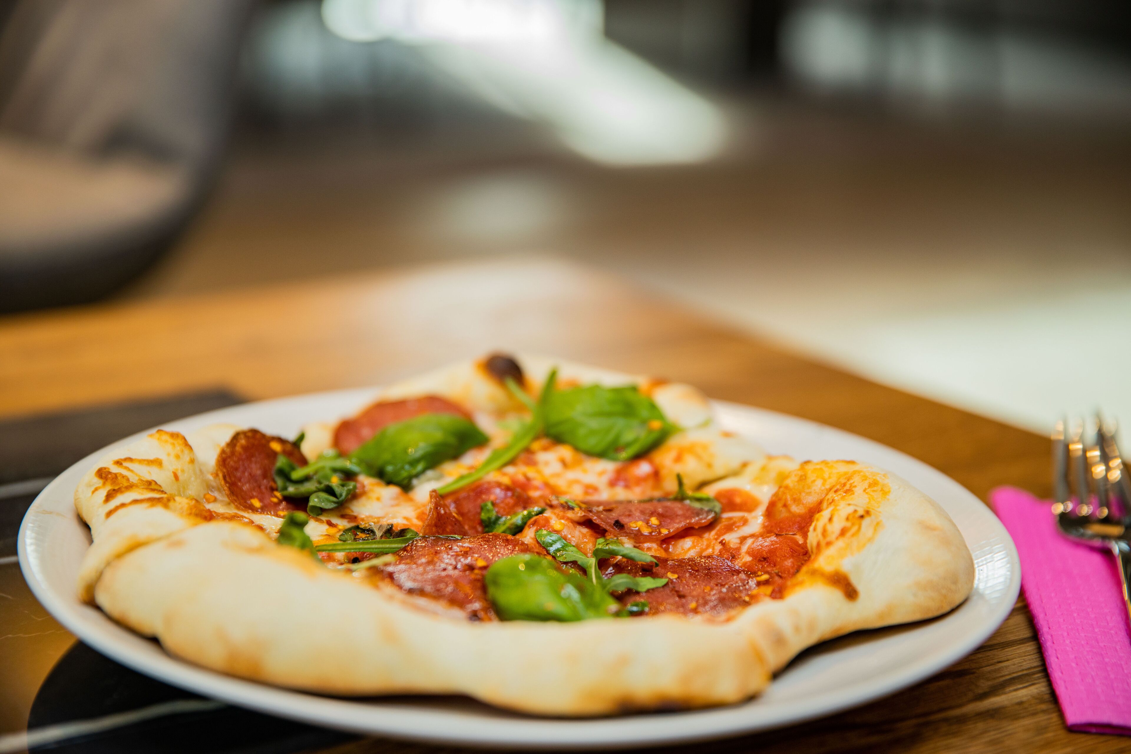 A pizza on a white plate with pepperoni and spinach on a wooden table.