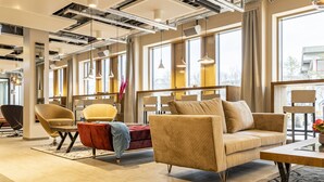 A modern lounge area with comfortable seating, large windows, and a contemporary ceiling design. - MASEVEN München Messe Dornach (Aschheim)