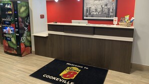 A reception area with a red wall, a framed welcome sign, a vending machine, and a Dell computer on the counter. - Super 8 by Wyndham Cookeville (Cookeville)