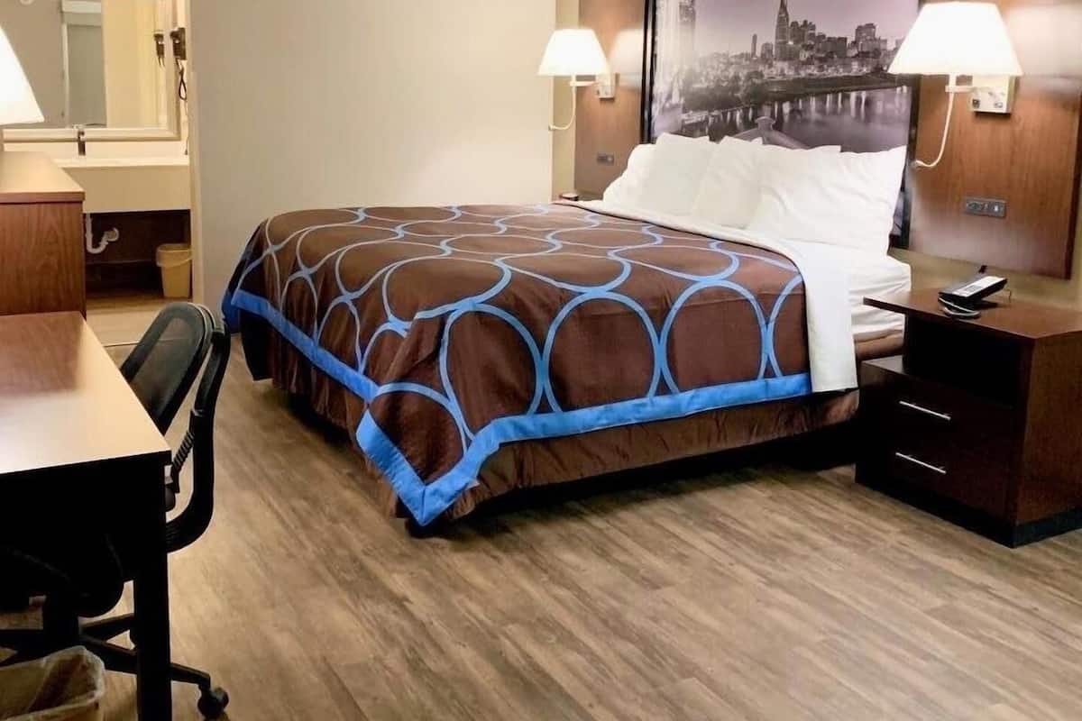 Une chambre d’hôtel comprenant un lit, un bureau, une chaise, une table de chevet, une lampe et un tableau accroché au mur.