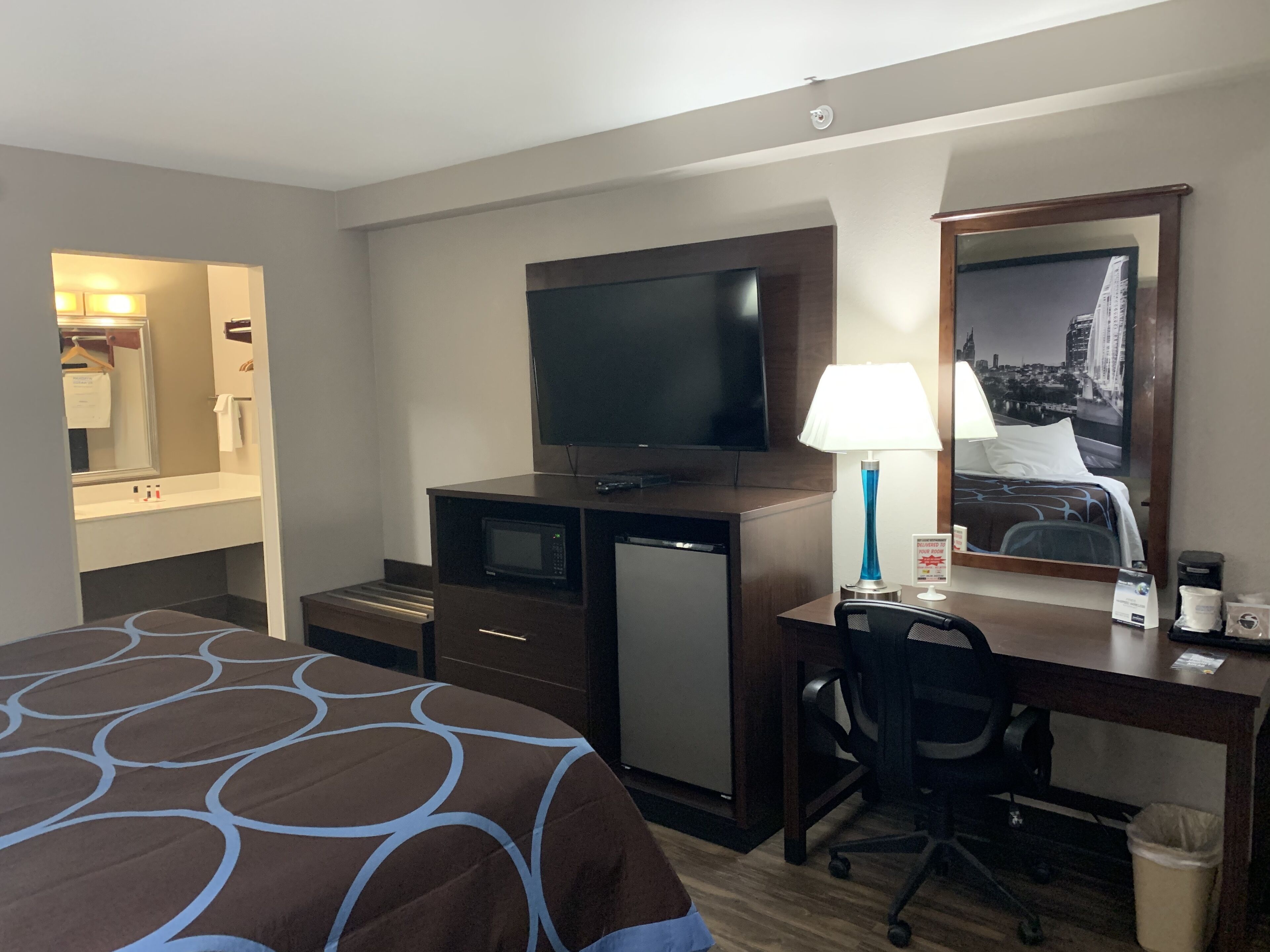 Une chambre d’hôtel équipée d’un lit, d’un bureau avec un ordinateur, d’une télévision, d’une lampe et d’une poubelle.
