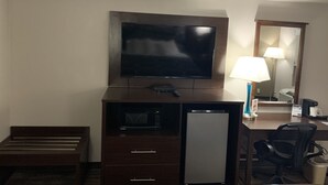 A hotel room with a flat-screen TV, a microwave, a mini-fridge, a desk with a lamp, a chair, and a trash can. - Super 8 by Wyndham Cookeville (Cookeville)