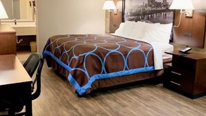 A hotel room with a bed, a desk, a chair, a nightstand, a lamp, and a large cityscape picture on the wall. - Super 8 by Wyndham Cookeville (Cookeville)