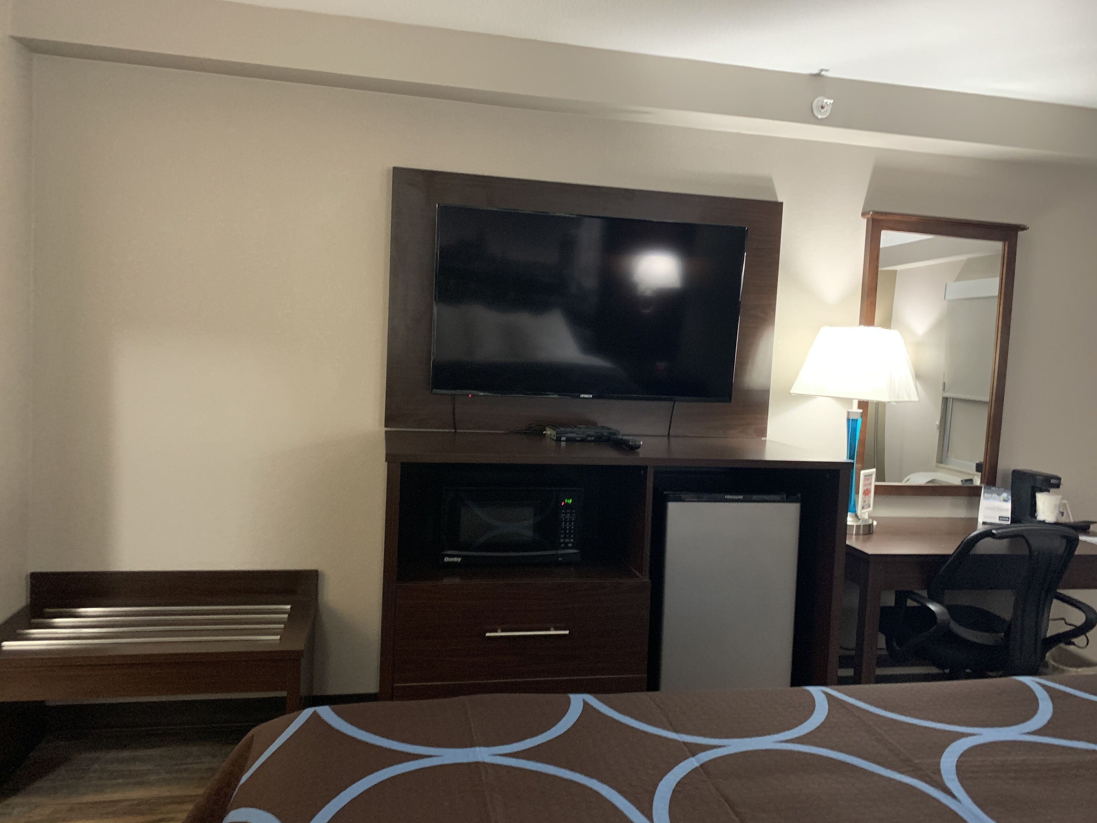 A hotel room with a bed, a desk with a television, a lamp, and a chair.