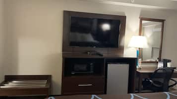 A hotel room with a bed, a desk with a television, a lamp, and a chair.