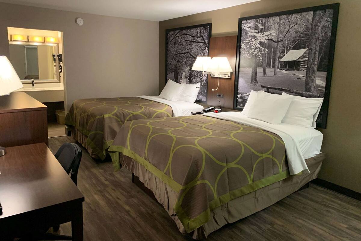 Une chambre d’hôtel avec deux lits, un bureau, une chaise, une lampe et un miroir.