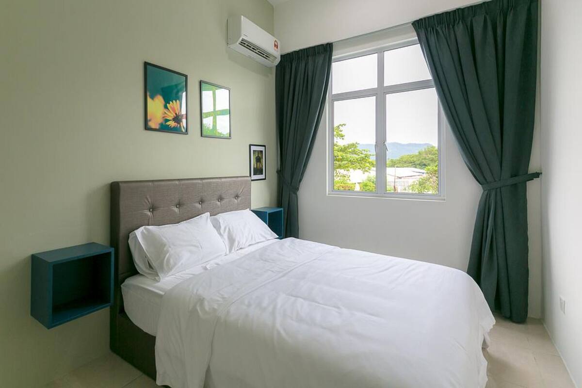 Un dormitorio con una cama, una mesita de noche, un ventanal con cortinas y dos cuadros colgados en la pared.