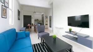 Un salon moderne avec un canapé, une table basse, un téléviseur et, au fond, un coin repas.