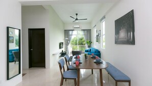 Un espace repas moderne avec une table ronde, des chaises et un banc. On y trouve un ventilateur de plafond, une fenêtre avec des rideaux et un tableau encadré au mur.