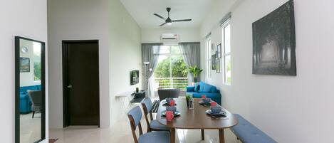 A modern dining area with a round table, chairs, and a bench. There is a ceiling fan, a window with curtains, and a framed picture on the wall.