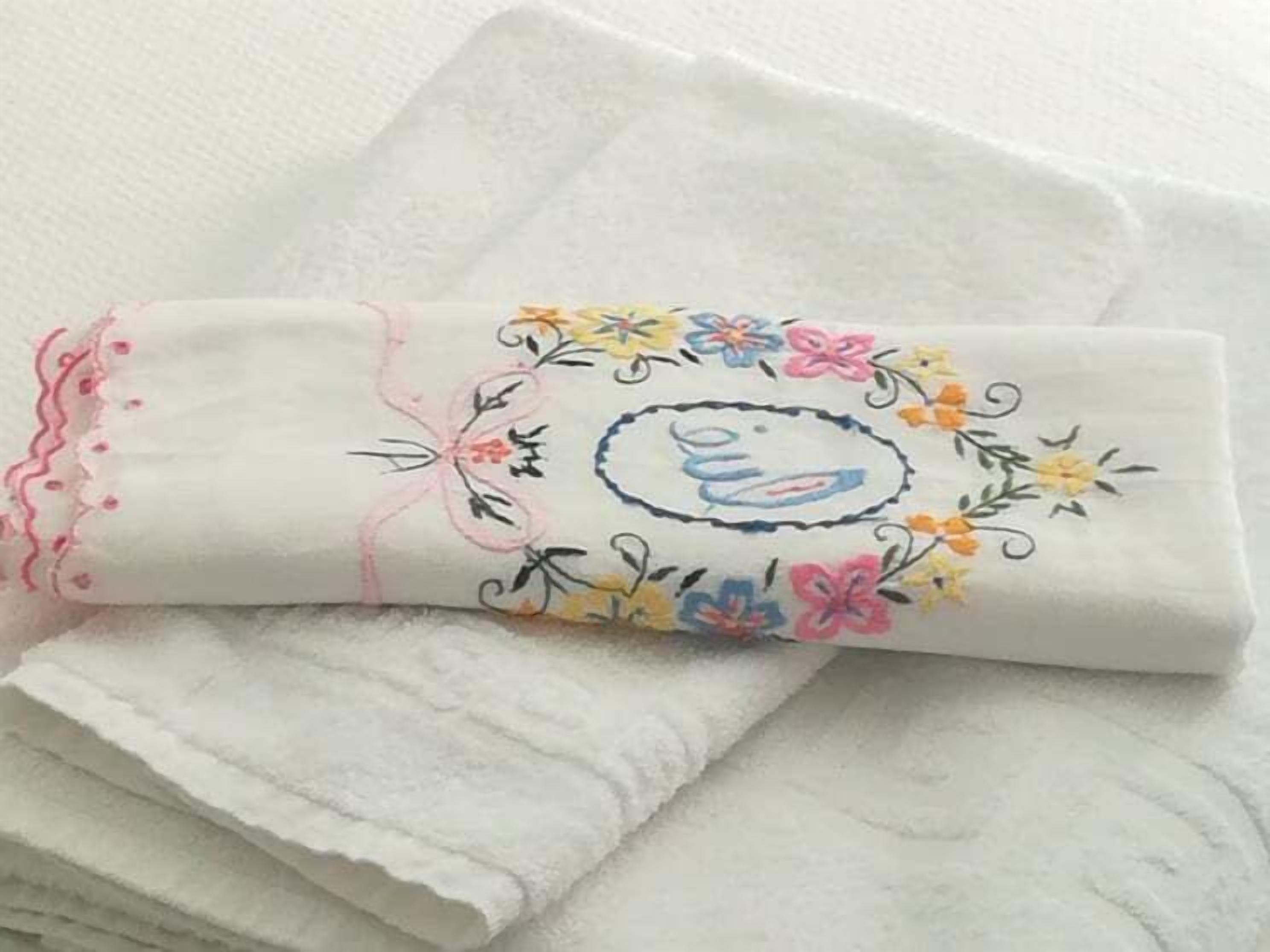 Een keurig gevouwen witte handdoek met geborduurde bloem- en vogelmotieven.