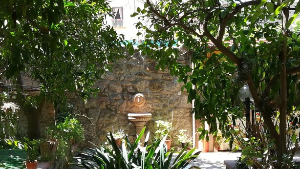 A courtyard with a stone wall, a fountain, and potted plants. - L'Aranceto Sorrentino Residence (Meta)