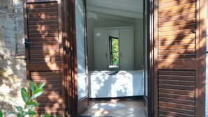 An open wooden door leading to a bedroom with a bed, a window, and a green mat at the entrance. - L'Aranceto Sorrentino Residence (Meta)