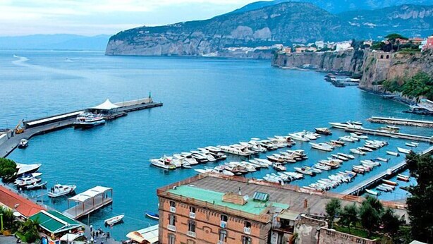 A coastal marina with boats docked, a pier extending into the water, and buildings along the shoreline. - L'Aranceto Sorrentino Residence (Meta)