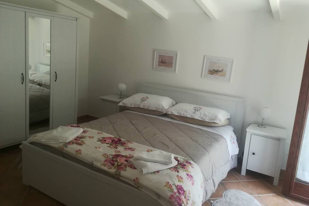 A bedroom with a bed, a wardrobe, a nightstand, and two wall-mounted pictures.
