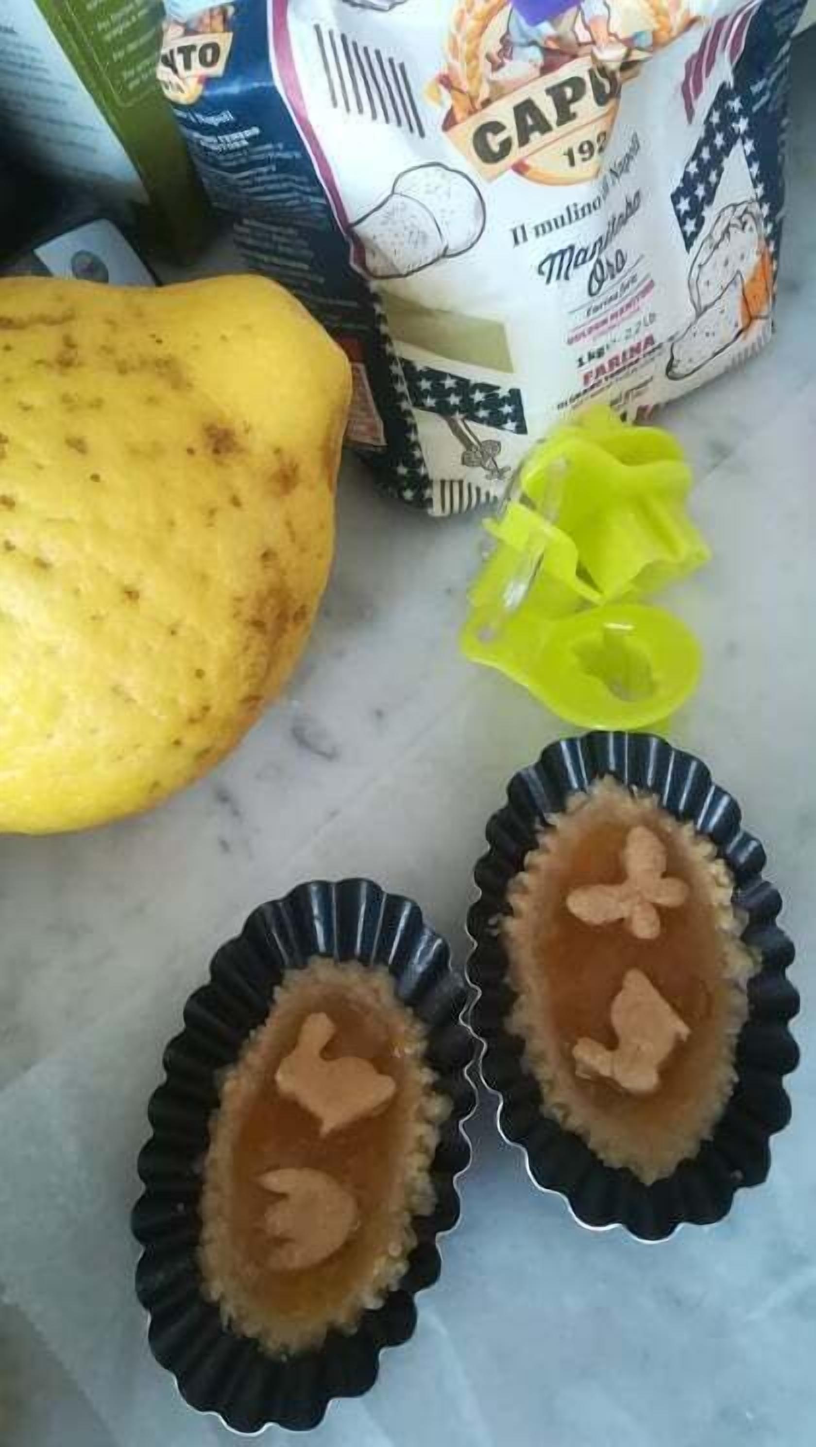 Una encimera de cocina con un calabacín amarillo, dos moldes para muffins con contenido marrón, y un saco de harina.