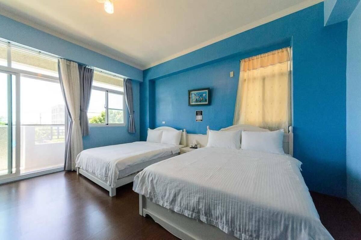 A hotel room with two beds, a large window with curtains, and a painting on the wall.