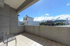 A balcony with a metal chair, a tiled floor, and a view of buildings and mountains in the distance. - Maji Homestay (Taitung)