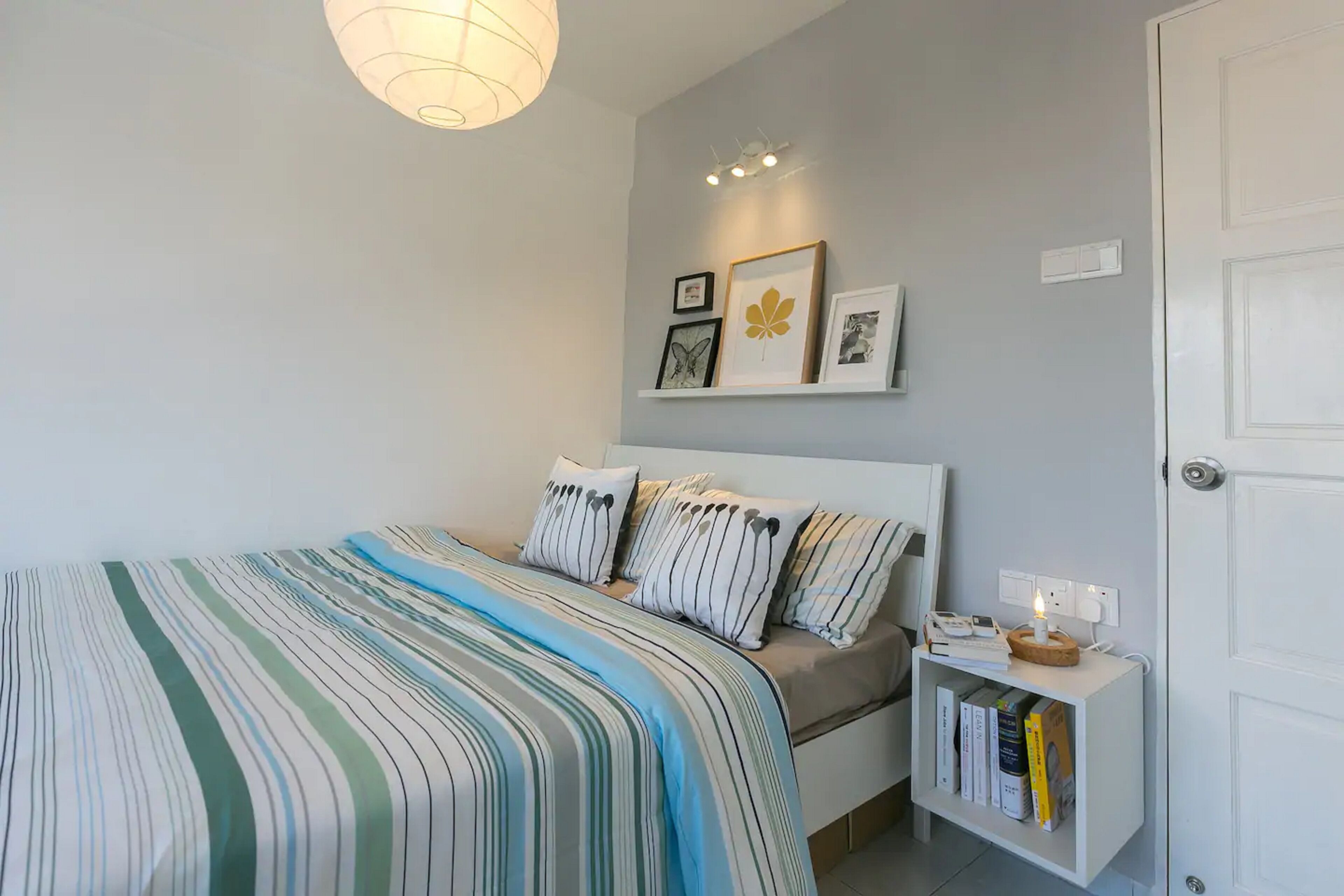 A bedroom with a bed, bedside table, and wall-mounted shelf with books and pictures.