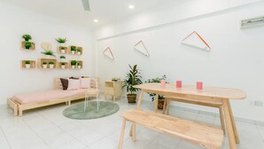 A minimalist room with a wooden bed, a round rug, a wooden bench, a table with pink candles, and several potted plants. - Eastern Court 22 by Sanguine (George Town)