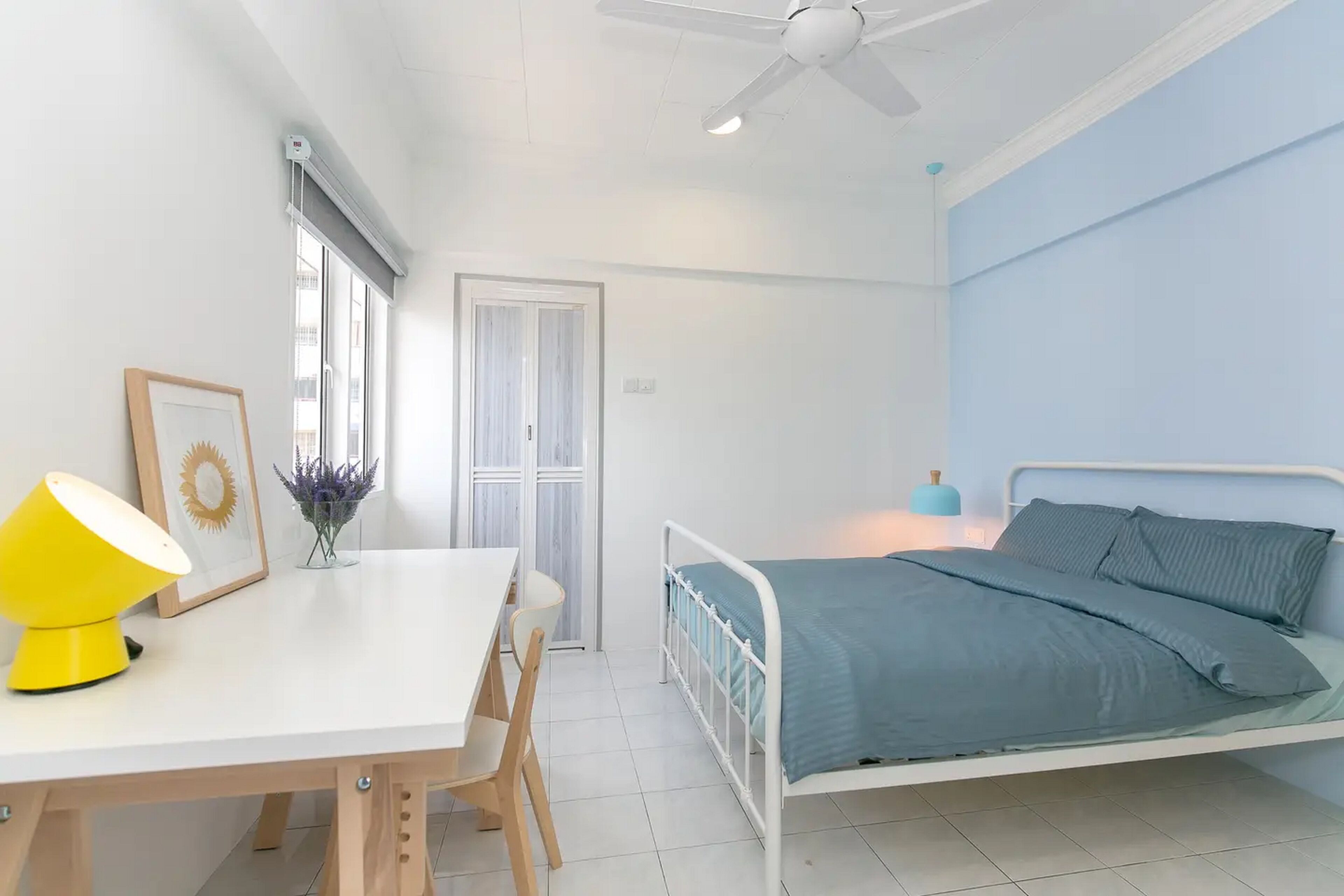 A bedroom with a bed, a desk with a chair, a ceiling fan, and a window with blinds.