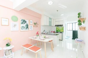 A modern kitchen with white cabinets, a green backsplash, and a dining area with a white table and orange cushions. - Desa Green Units by Sanguine (George Town)