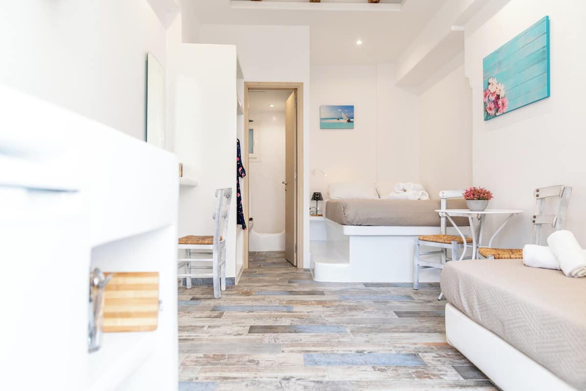 A modern, well-lit room with a bed, a small table with a chair, a painting on the wall, and a wooden floor.