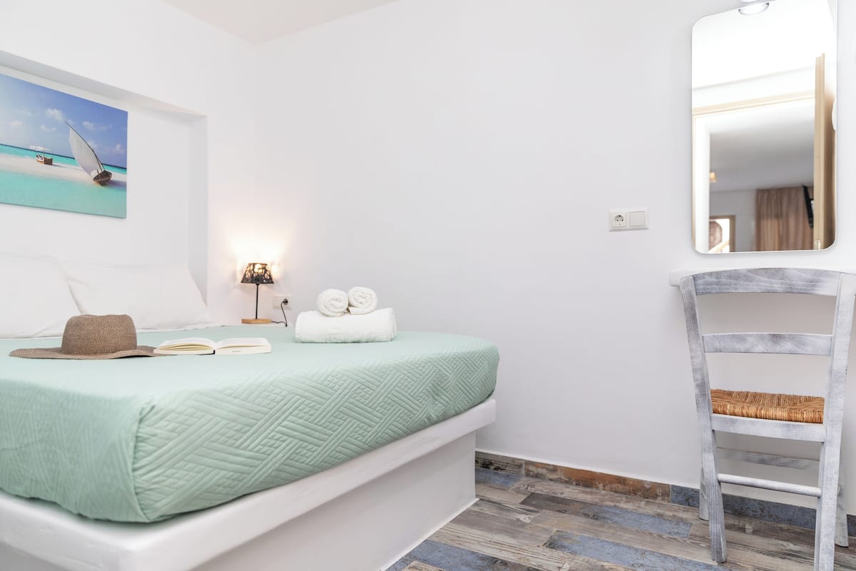 A bedroom with a bed, a bedside lamp, a painting, and a wooden chair.