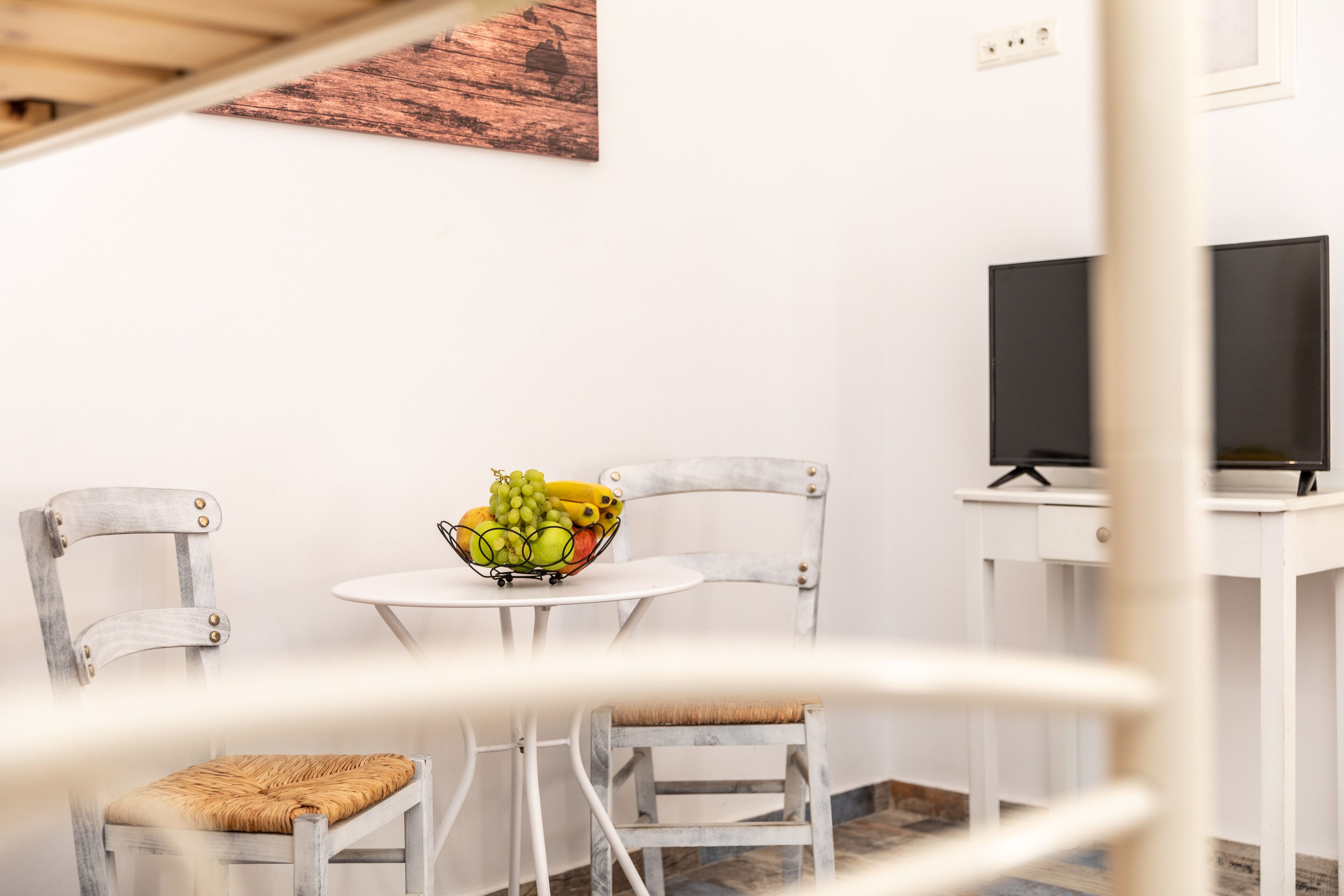 A dining area with a table, two chairs, a fruit bowl, and a TV on a stand.