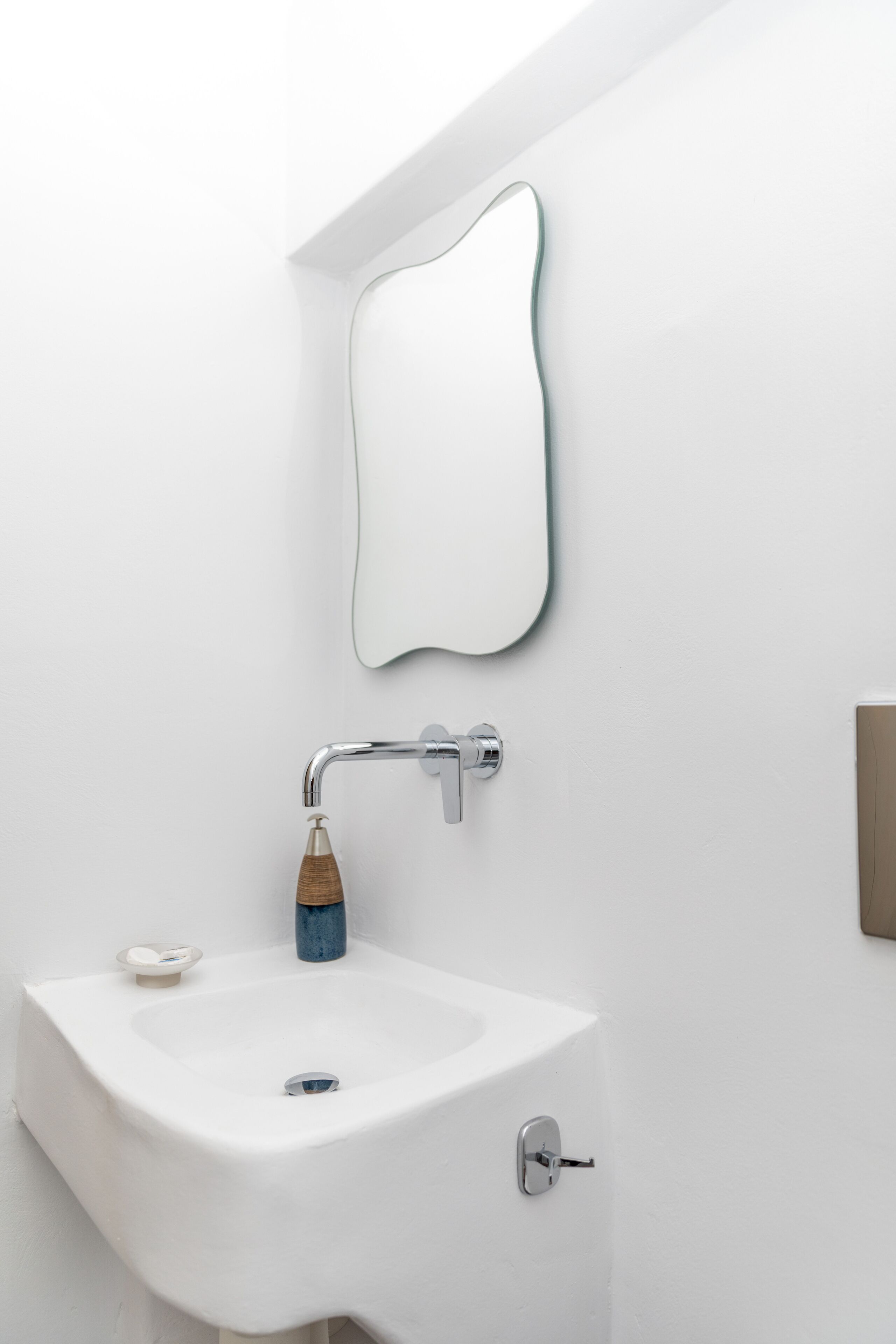 Ein modernes Badezimmer mit einem weißen Waschbecken, einem hölzernen Seifenspender und einem Spiegel an der Wand.