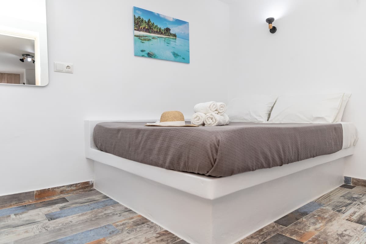 A modern bedroom with a white bed, a beach-themed wall art, and a wooden floor.