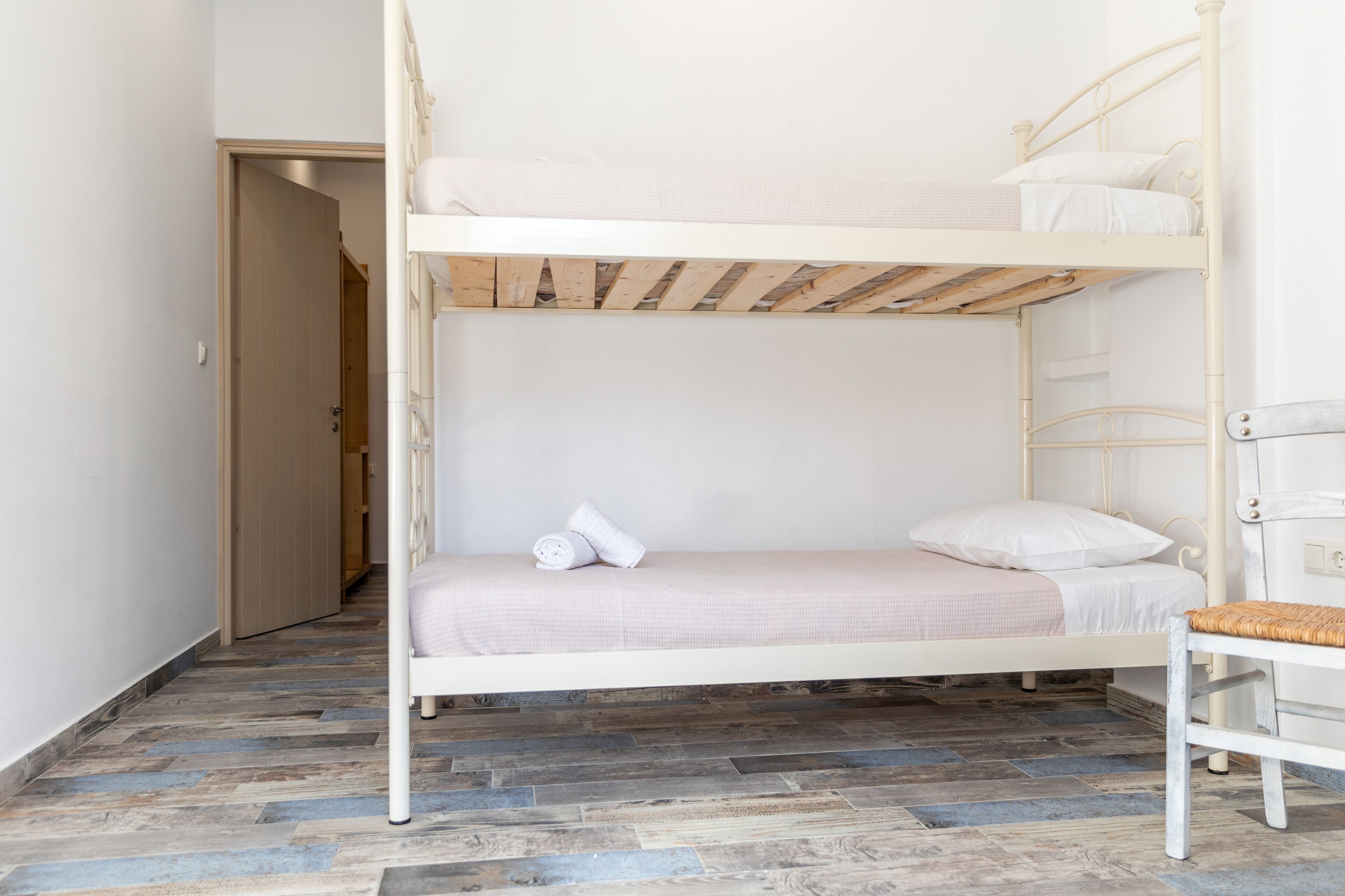 A bunk bed with a wooden ladder, a white chair, and a wooden door in the background.