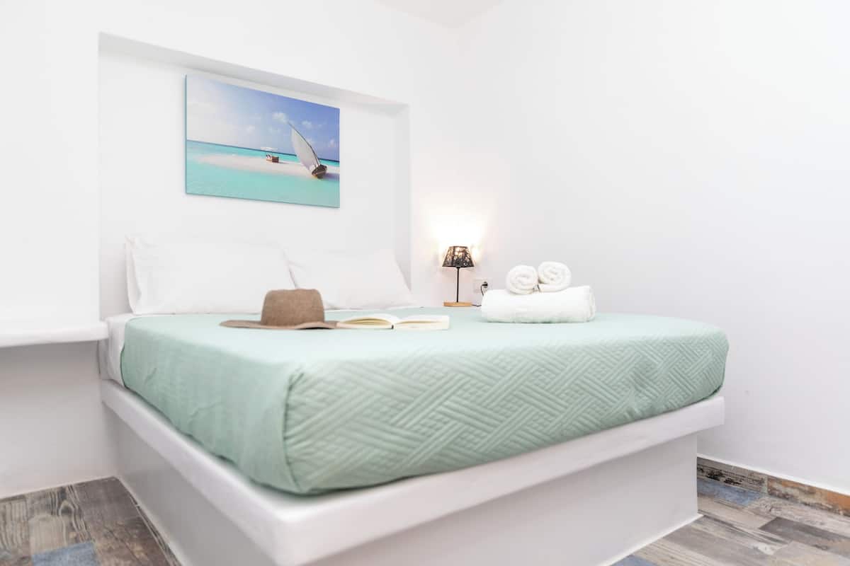 A bedroom with a bed, a painting of a beach scene, a lamp, and a pair of towels.