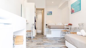 Una habitación moderna y bien iluminada con una cama, una pequeña mesa con una silla, un cuadro en la pared y piso de madera.