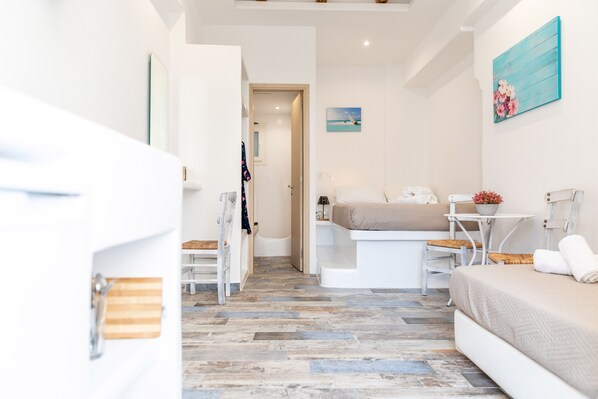 A modern hotel room with a bed, a small table, a chair, and a bathroom visible through an open door.