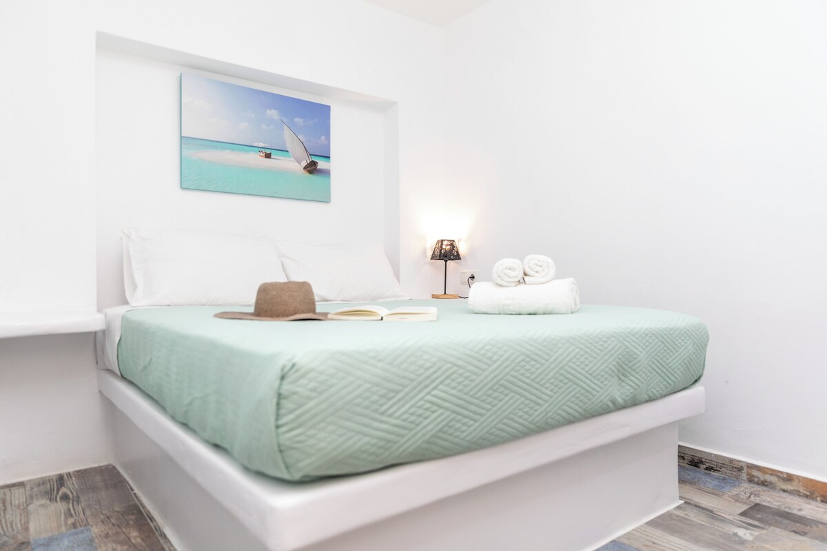 Un dormitorio con una cama, un cuadro de una playa, una lámpara y un par de toallas.