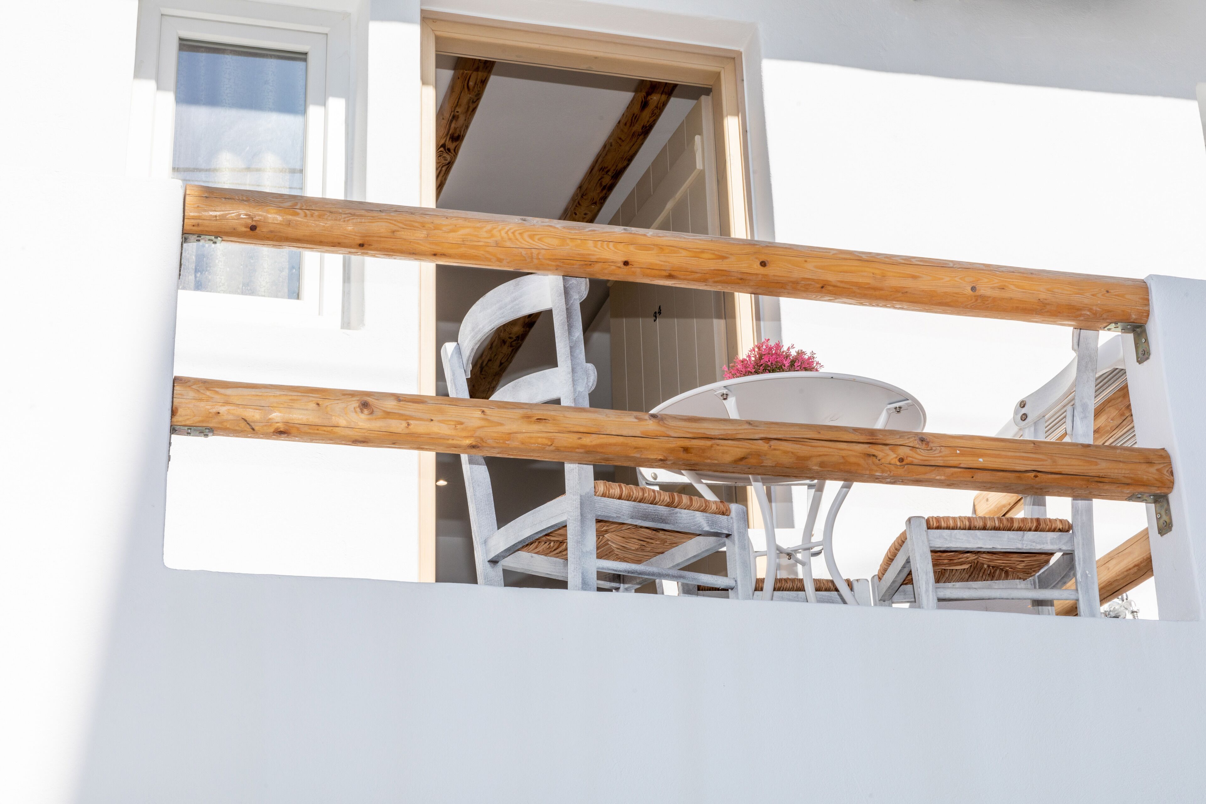 A balcony with a wooden railing, a white table, and wicker chairs.