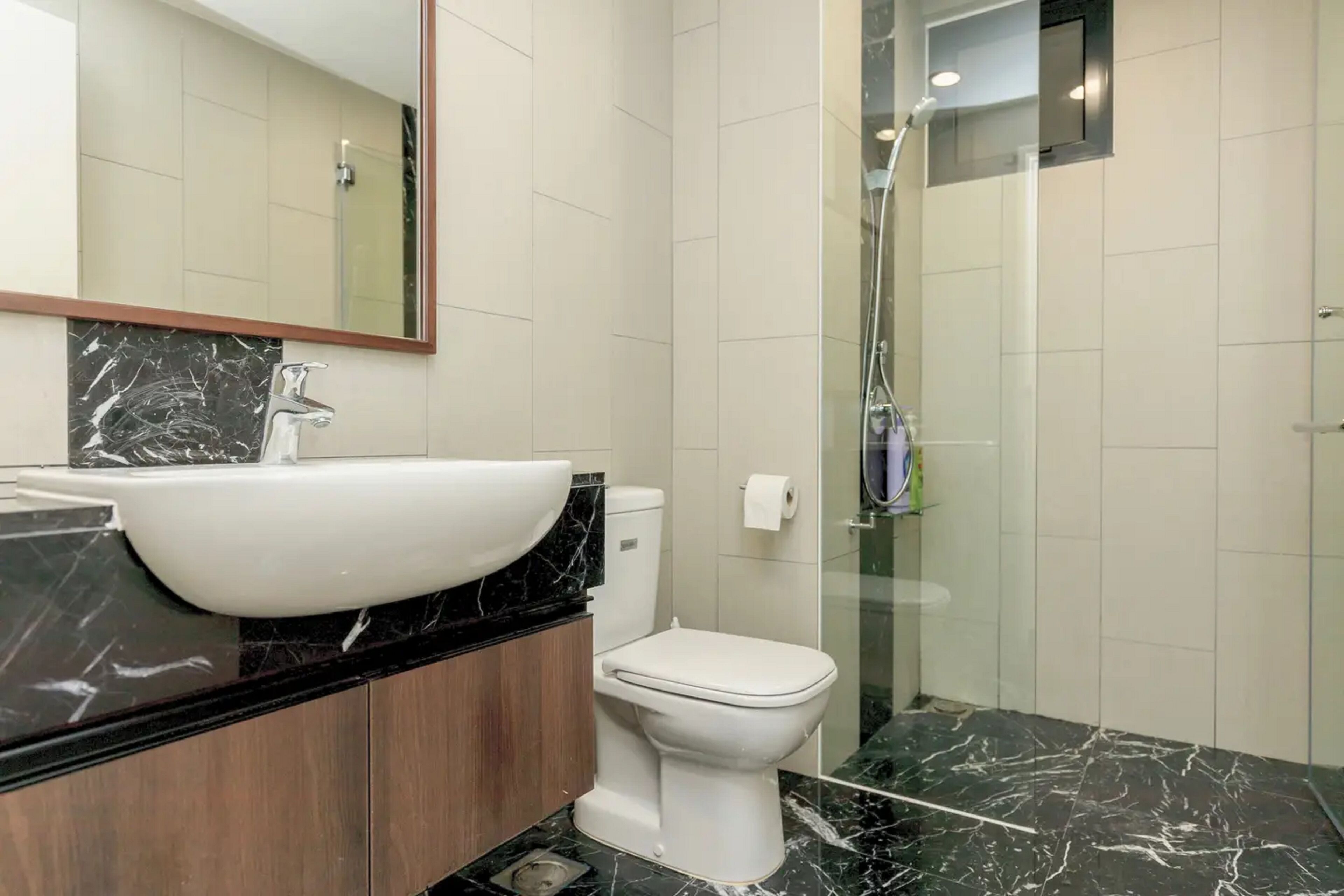 A modern bathroom with a large white sink, a toilet, and a glass-enclosed shower.