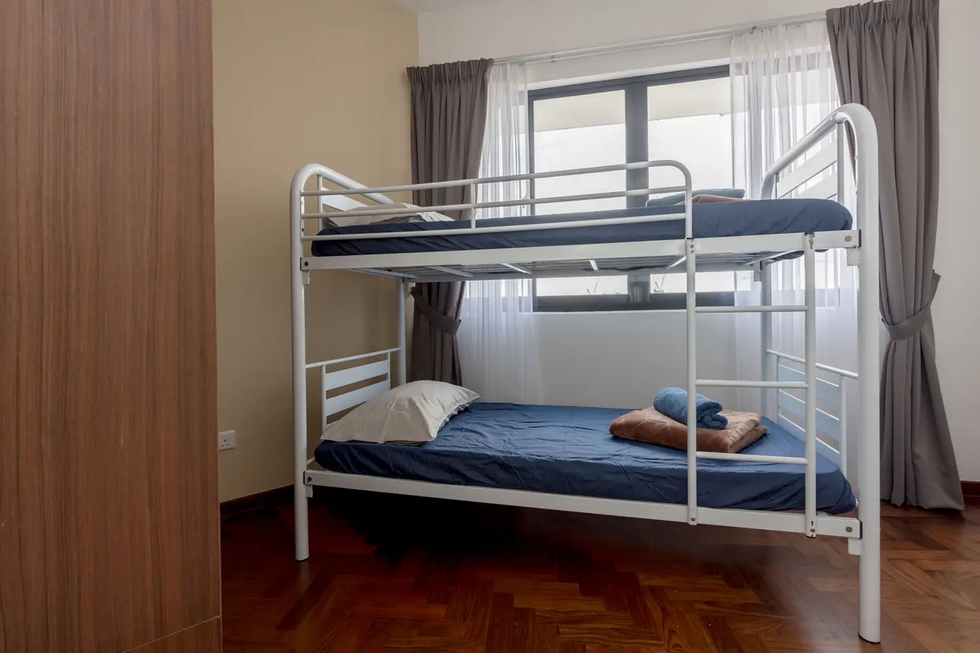 A bunk bed with a window and curtains, wooden flooring, and a wall with a wooden panel.